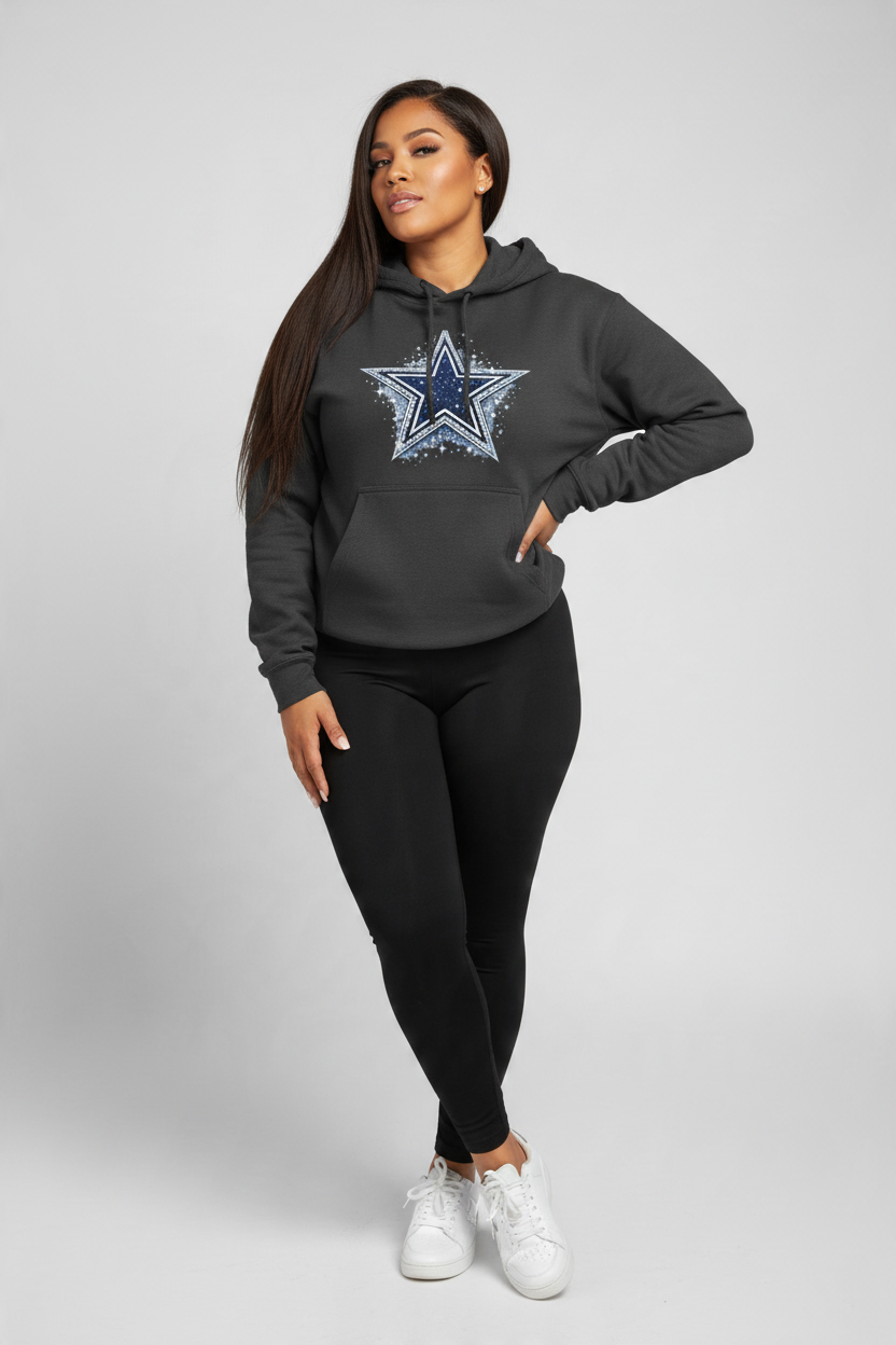 A woman modeling a dark gray hoodie with a distressed Dallas Cowboys star logo on the chest, paired with black leggings and white sneakers, against a light gray studio background.